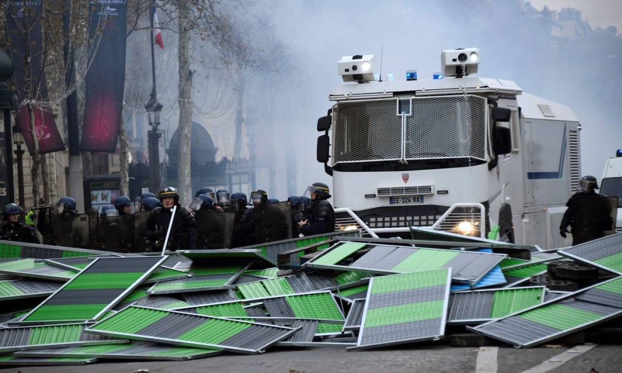 Integrantes da polícia antimotim se posicionam atrás de uma barricada durante um protesto dos coletes amarelos nos Champs-Elysées. A polícia disparou gás lacrimogêneo e canhões de água contra os manifestantes Foto: BERTRAND GUAY / AFP