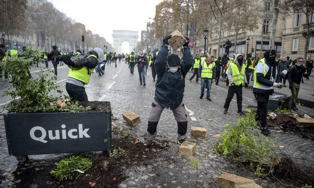 Um manifestante segura uma pedra ao lado de um vaso de flores danificado na avenida dos Champs-Elysées, durante uma manifestação nacional iniciada pelos coletes amarelos para protestar contra o aumento dos preços do petróleo e os custos de vida Foto: LUCAS BARIOULET / AFP