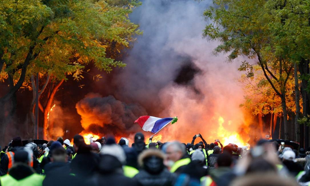 Manifestante agita a bandeira da França diante de pilha de pneus queimados em Paris, durante manifestação dos coletes amarelos Foto: GEOFFROY VAN DER HASSELT / AFP
