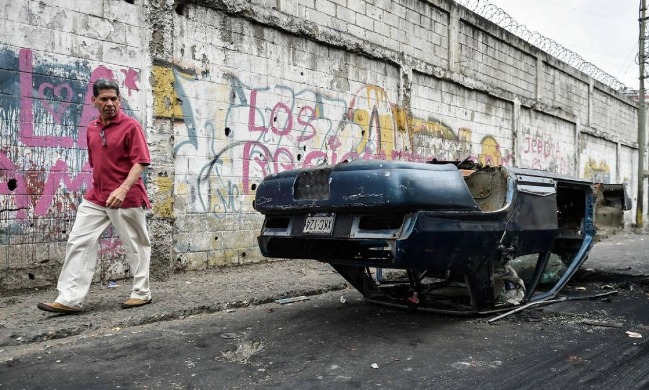 Homem passa ao lado de carro virado durante madrugada de protestos e violência na Venezuela; marchas têm sido convocadas por líder opositor Juan Guaidó, presidente do Parlamento Foto: LUIS ROBAYO / AFP