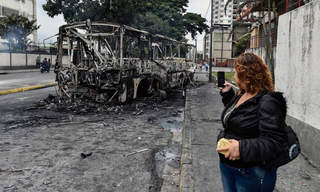 Mulher tira foto de um ônibus queimado em Caracas na véspera de jornada de marchas convocada pela oposição venezuelana Foto: LUIS ROBAYO / AFP