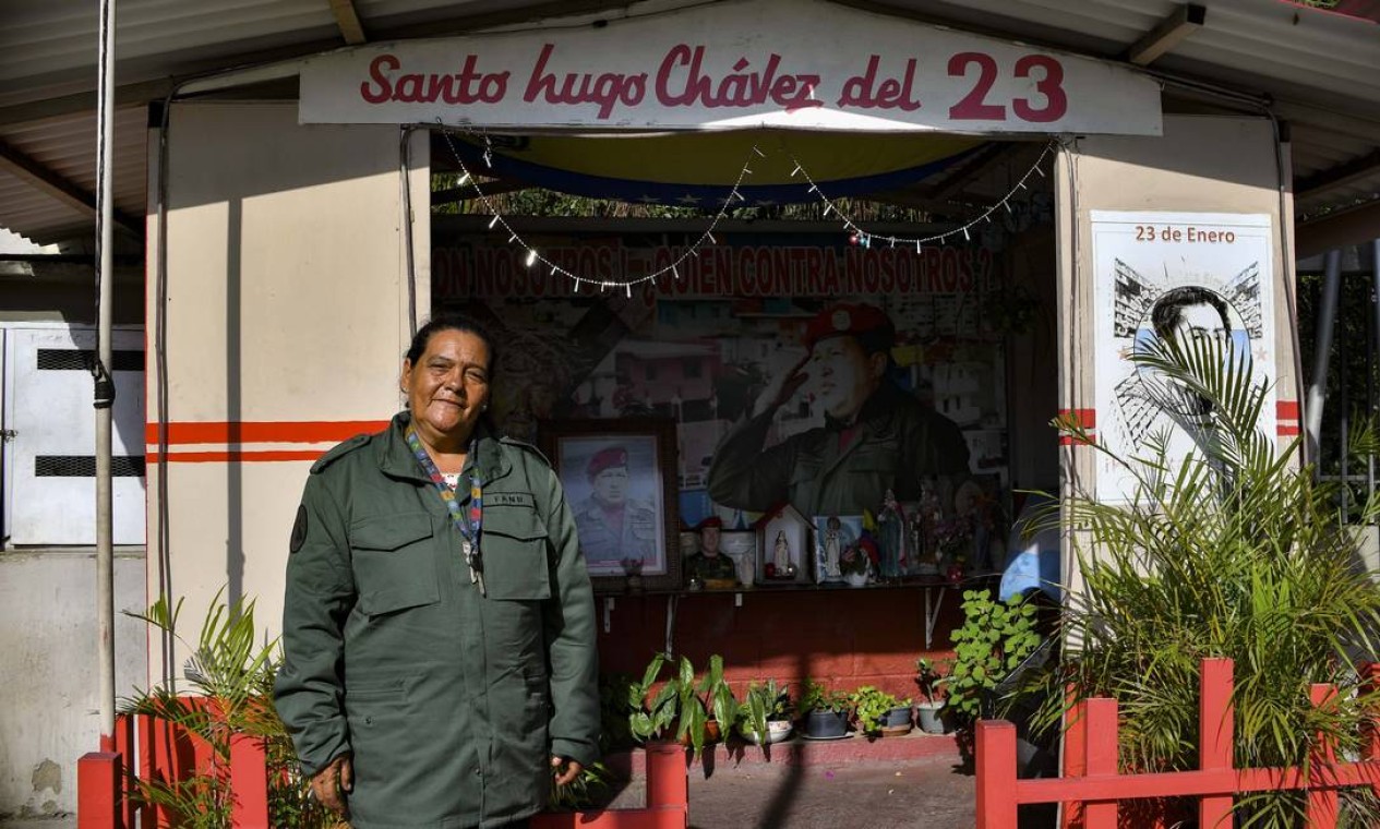 Uma mulher posa para foto em frente à capela em homenagem a Hugo Chávez, no bairro 23 de Janeiro, em Caracas. O cartaz chama o falecido presidente de santo Foto: YURI CORTEZ / AFP