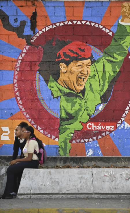 Imagens de Chávez são encontradas em vários pontos da capital. Estudantes se sentam ao lado de grafite com imagem de Chávez no bairro 23 de Janeiro Foto: YURI CORTEZ / AFP