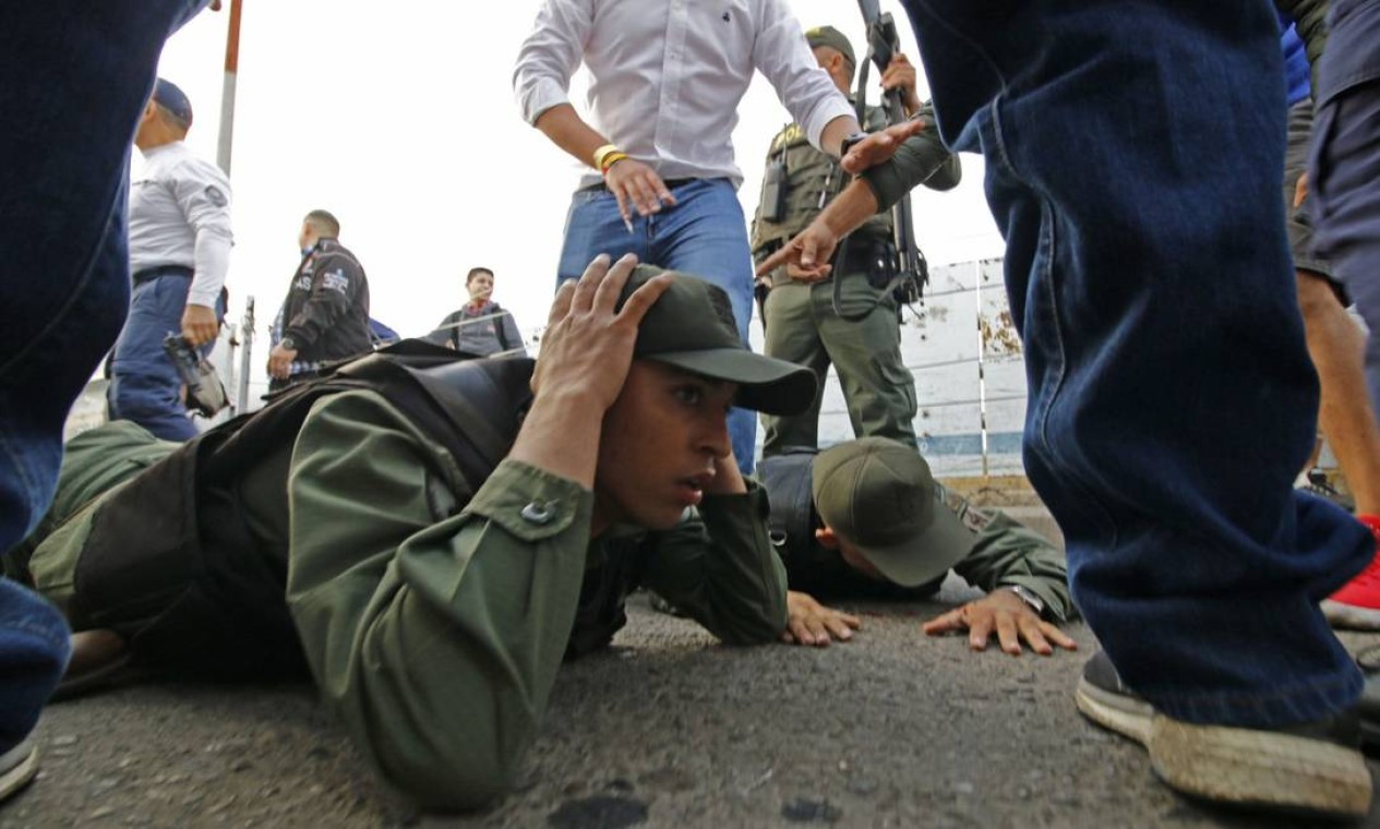Dois soldados venezuelanos se deitam no chão ao se entregarem à polícia colombiana em Cúcuta, após atravessarem a ponte Simón Bolívar em blindados; 23 militares desertaram Foto: SCHNEYDER MENDOZA / AFP