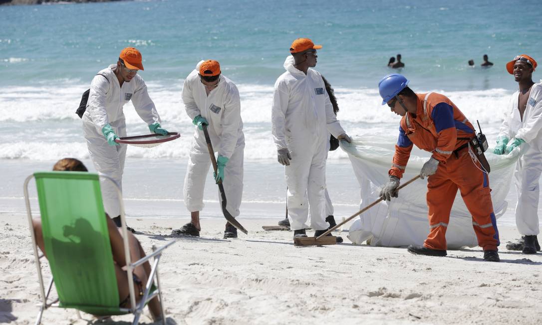 Banhista observa o trabalho de limpeza do material nesta sexta-feira em Arraial do Cabo Foto: Marcio Alves / Agência O Globo