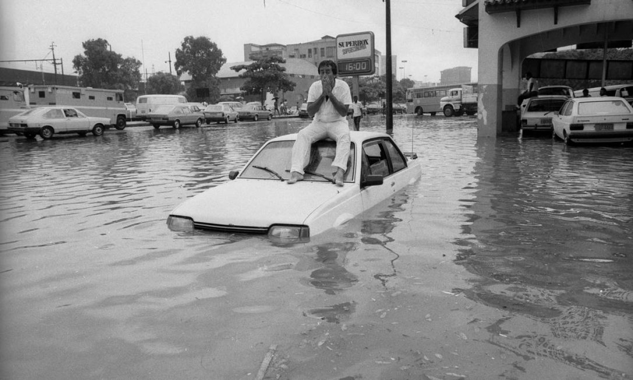 Fevereiro de 1986. Motorista espera a água da chuva baixar sentado sobre o teto de seu carro, na Praça da Bandeira Foto: Anibal Philot / Agência O Globo