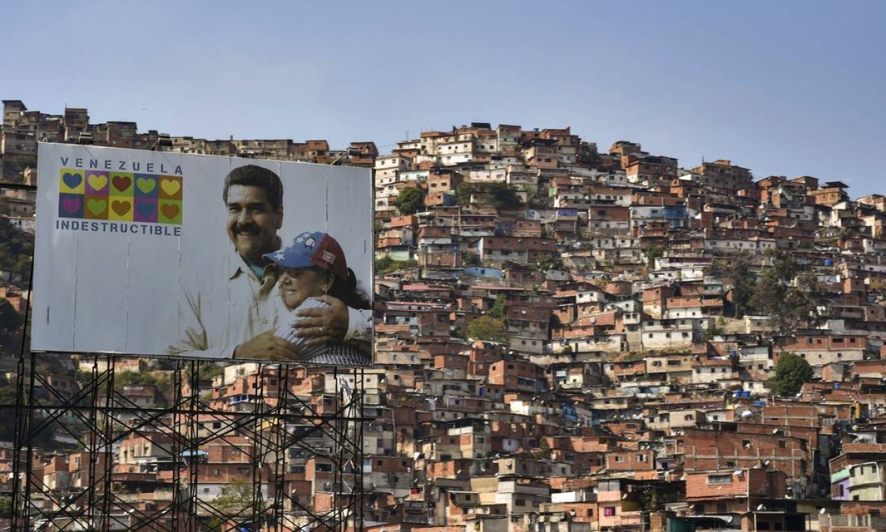 Placa mostra o presidente Nicolás Maduro abraçado à sua mulher, Cilia Flores, com os dizeres 'Venezuela Indestrutível', e, ao fundo, se vê uma das favelas de Caracas; pobres são os mais afetados pela crise humanitária Foto: YURI CORTEZ / AFP