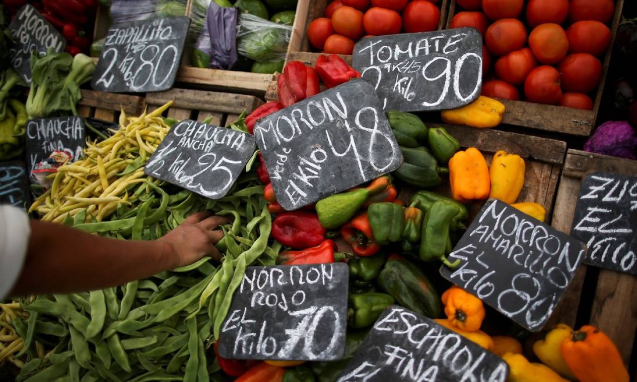 Um vendedor de vegetais pega um punhado de feijão indiano em uma feira de rua, em Buenos Aires. Governo prevê congelar preços de produtos essenciais e de serviços públicos Foto: AGUSTIN MARCARIAN / REUTERS