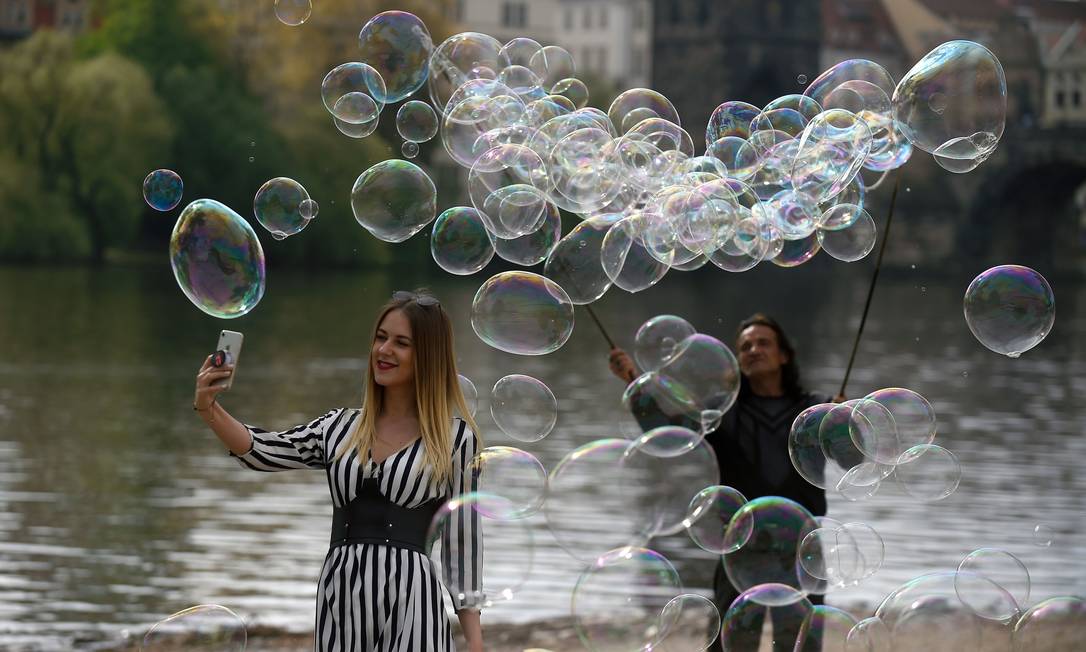 Uma turista faz selfie enquanto um artista faz bolhas de sabão na margem do rio Vltava, em Praga, República Checa Foto: MICHAL CIZEK / AFP