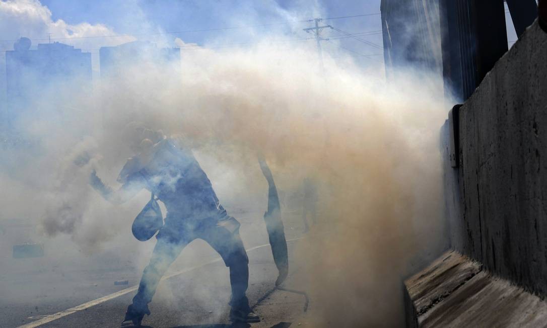 Manifestantes usam máscaras e tecidos para se protegerem do gás e revidam os soldados com pedras. Uma parte dos militares uniu-se à tentativa de derrubar o governo de Maduro. Em vídeo postado às 5h47 locais (6h47 no Brasil), Guaidó apareceu cercado de militares, afirmando que "valentes soldados acudiram ao nosso chamado" e conclamando a população a ir às ruas Foto: YURI CORTEZ / AFP
