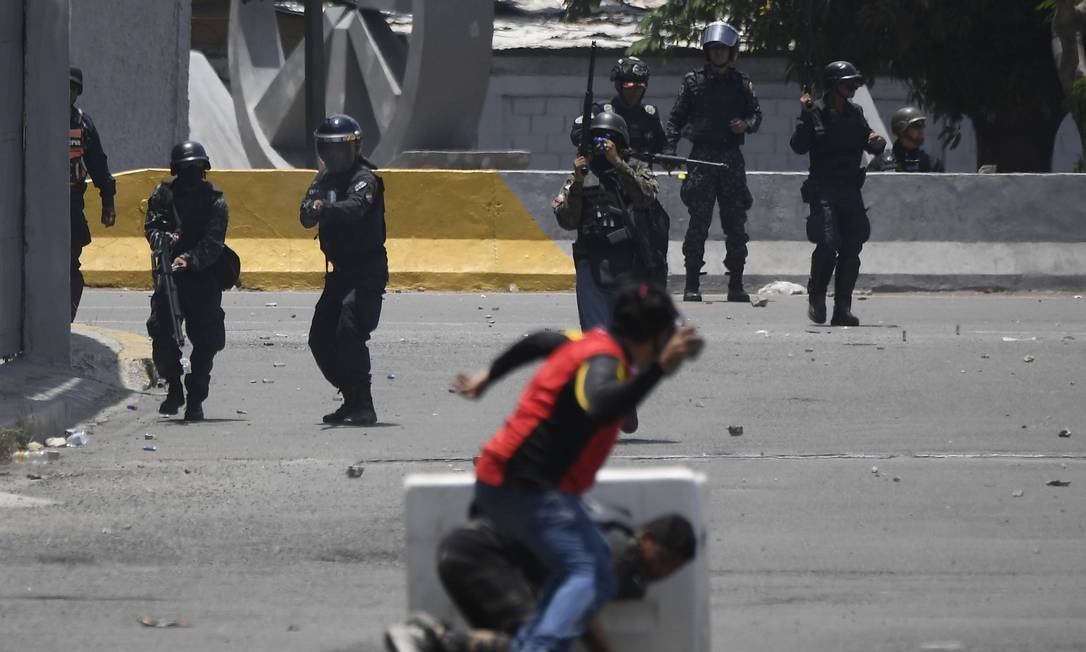 Apoiadores de Guaidó revidam os soldados com pedras, enquanto alguns tentam se proteger. Conflitos ocorrem nos arredores da base militar La Carlota, em Caracas. Blindados atropelaram manifestantes Foto: FEDERICO PARRA / AFP