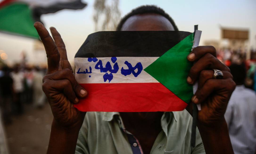 
Manifestante sudanês segura a bandeira do país com os dizeres ‘apenas civis’ escritos em árabe em protesto do lado de fora da sede do Ministério da Defesa em Cartum: pressão por novo conselho de transição com participação civil
Foto:
ASHRAF SHAZLY/AFP/02-05-2019
