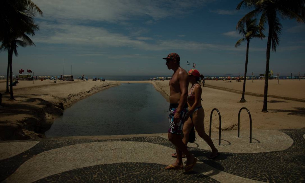 Casal passeia pelo calçadão de Copacabana, ao lado da enorme língua-negra que enfeia a paisagem da praia Foto: Brenno Carvalho / Agência O Globo