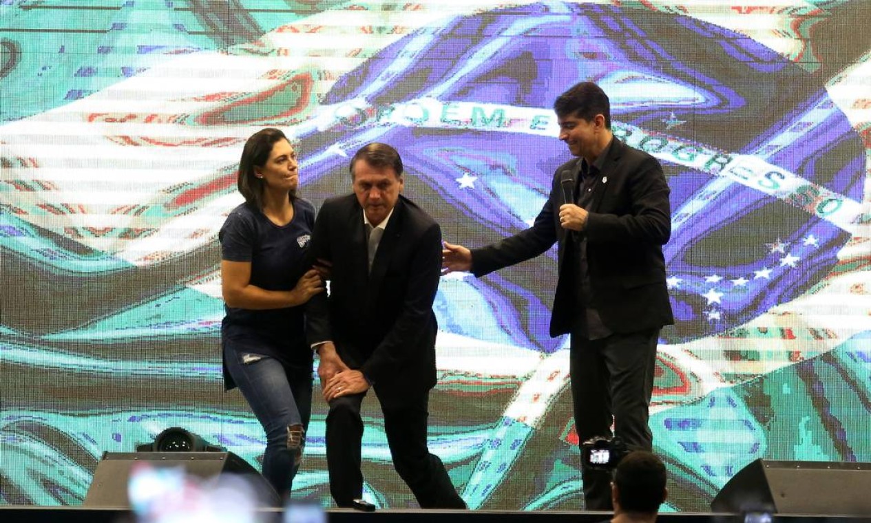 A primeira-dama Michelle Bolsonaro ajuda o presidente a levantar após a oração Foto: Fabiano Rocha / Agência O Globo