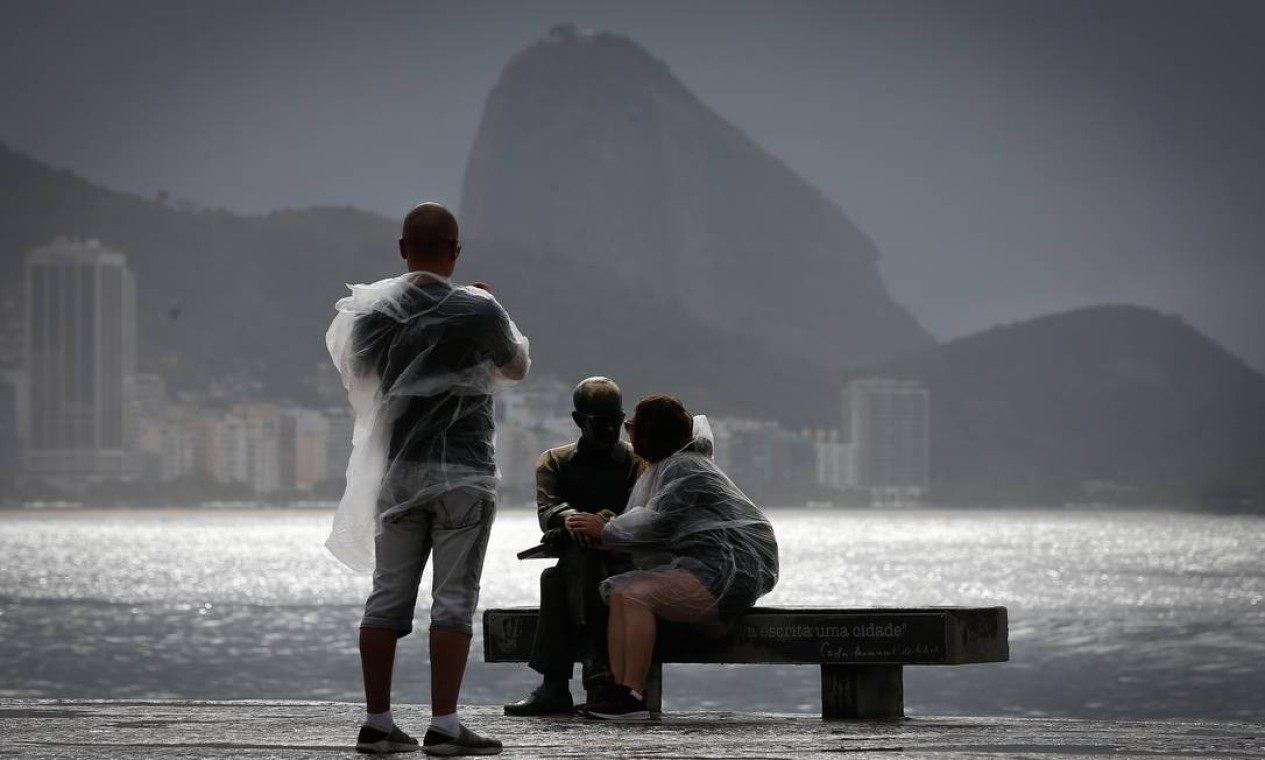 Em dia de chuva, turistas protegidos por capa tiram foto com a estátua de Drummond em Copacabana Foto: Pablo Jacob / Agência O Globo