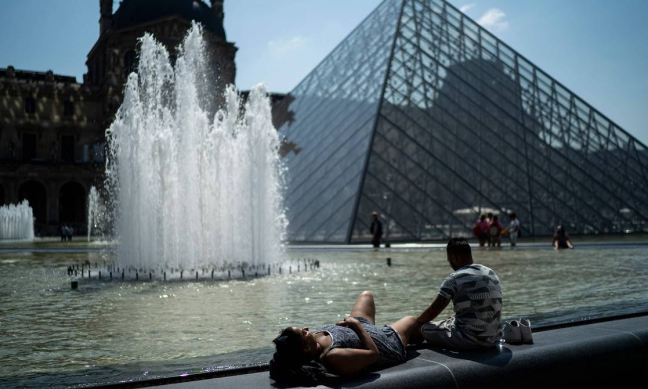 Pessoas tomam banho de sol em frente à pirâmide do Louvre durante onda de calor em Paris Foto: KENZO TRIBOUILLARD / AFP
