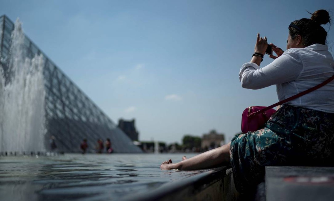 Mulher mergulha os pés em fonte perto da pirâmide do Louvre, em Paris. Segundo meteorologistas, onda de calor "sem precedentes" atinge grande parte da Europa Ocidental neste mês de junho Foto: KENZO TRIBOUILLARD / AFP