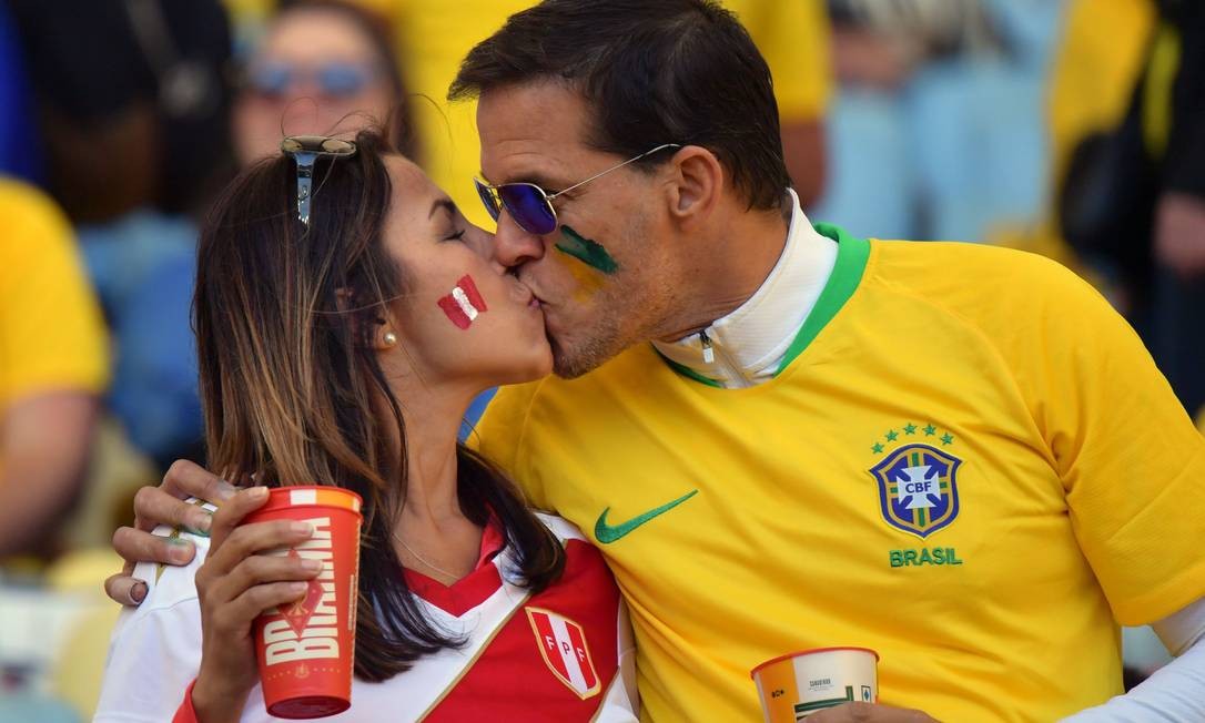 Opostos apaixonados. Casal de torcedores se beija antes do início da partida final da Copa América entre Brasil e Peru, no Maracanã Foto: LUIS ACOSTA / AFP