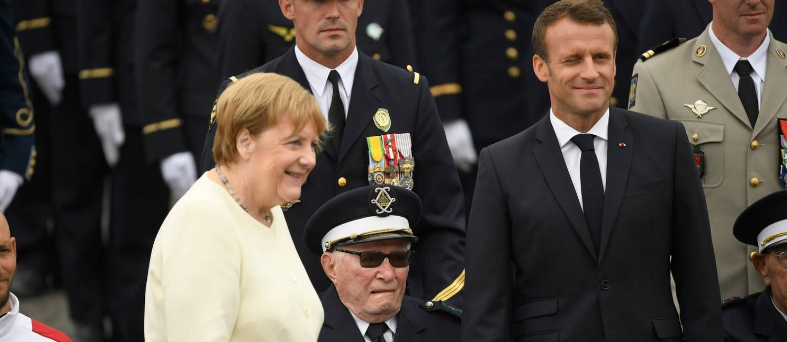 O presidente francês, Emmanuel Macron, e a chanceler alemã, Angela Merkel, posam com um veterano da Segunda Guerra, no desfile pelos 230 anos da Queda da Bastilha, na avenida Champs-Elysées, na capital francesa Foto: LIONEL BONAVENTURE / AFP