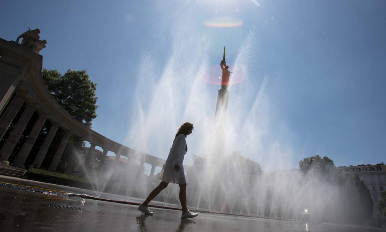 Mulher passa por água pulverizada de um cano na praça Schwarzenberg, em frente ao monumento do Exército Vermelho, em Viena, na Áustria Foto: ALEX HALADA / AFP