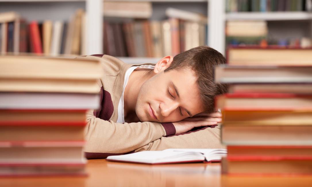 SOC -- USO EXCLUSIVO DE SOCIEDADE USO LIMITADO Sleeping at the library. Tired young man sleeping near the book stacks at the library SONO ESTUDO Foto: Reprodução