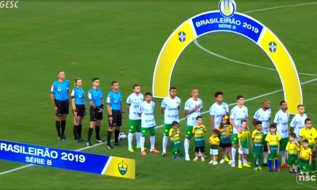Arbitragem e jogadores do Cuiabá ouvem o Hino Nacional sem a equipe do Figueirense Foto: Picasa / Reprodução de TV