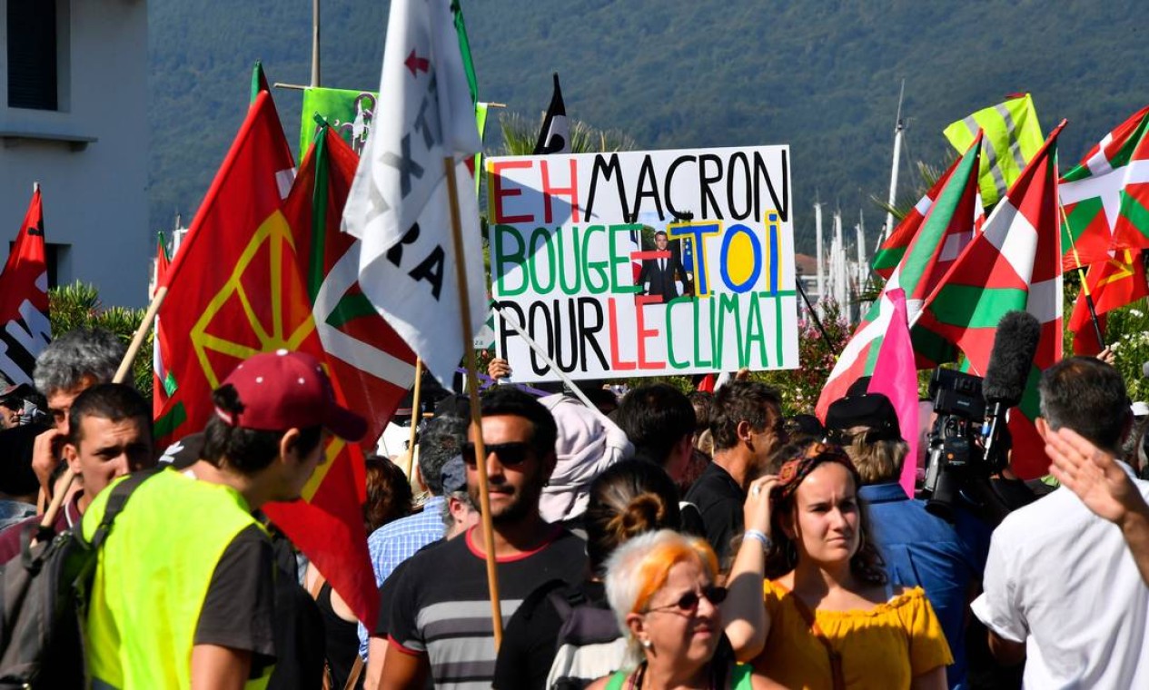 Um manifestante segura um cartaz com a frase "Ei Macron, mova-se pelo clima" enquanto outros seguram bandeiras bascas durante protesto na França Foto: Georges Gobet / AFP