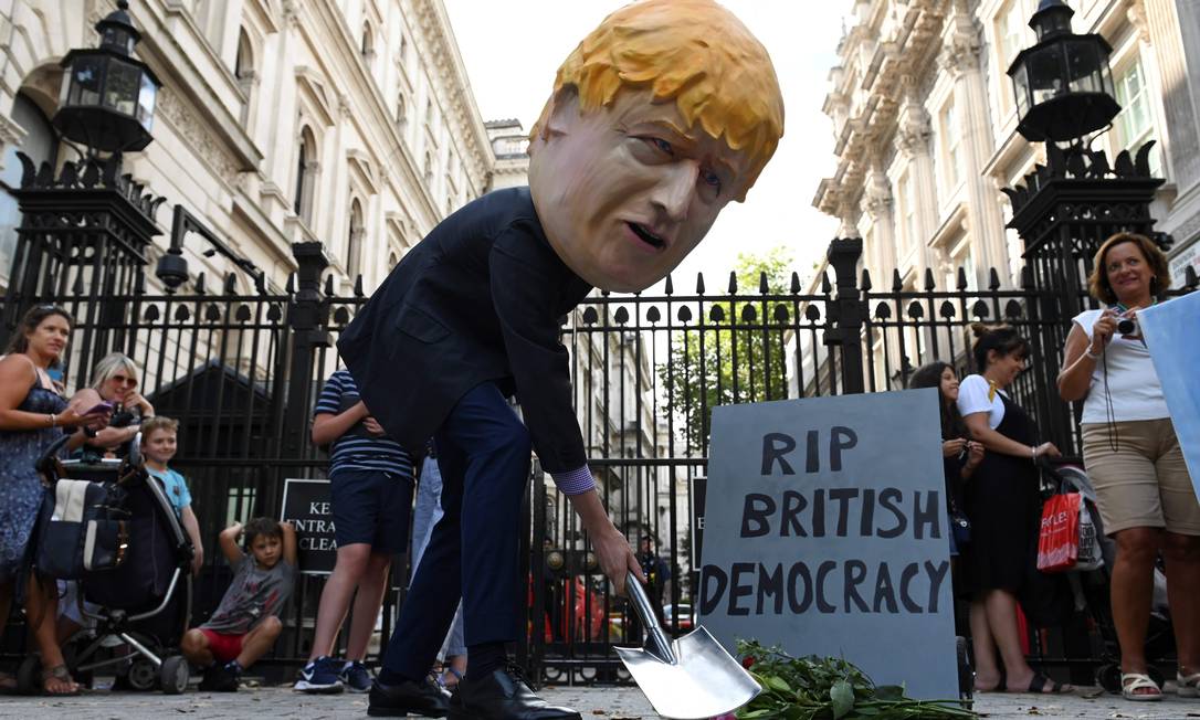 Manifestante usando máscara do premier Boris Johnson encena o que seria o jazigo da democracia no Reino Unido. Oposição e parte do Partido Conservador consideram que suspensão do Parlamento violou as leis do país Foto: DANIEL LEAL-OLIVAS / AFP