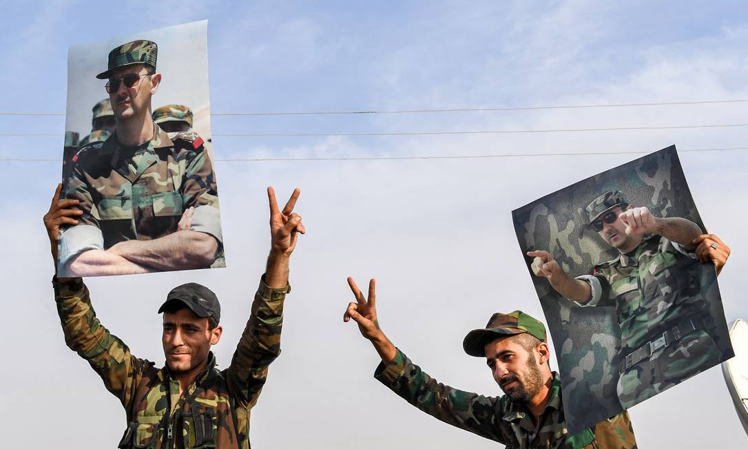 Militares sírios levantam fotos do presidente Bashar al-Assad. Anúncio de cessar-fogo no Nordeste do país foi recebido com otimismo e cautela pelo governo, que apoia as milícias curdas contra a Turquia Foto: - / AFP