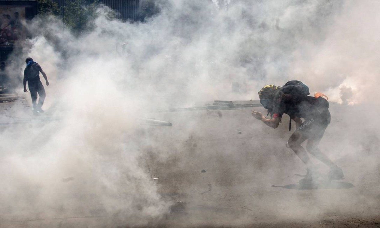 Fumaça do gás lacrimogêneo encobre os manifestantes na capital chilena Foto: CLAUDIO REYES / AFP
