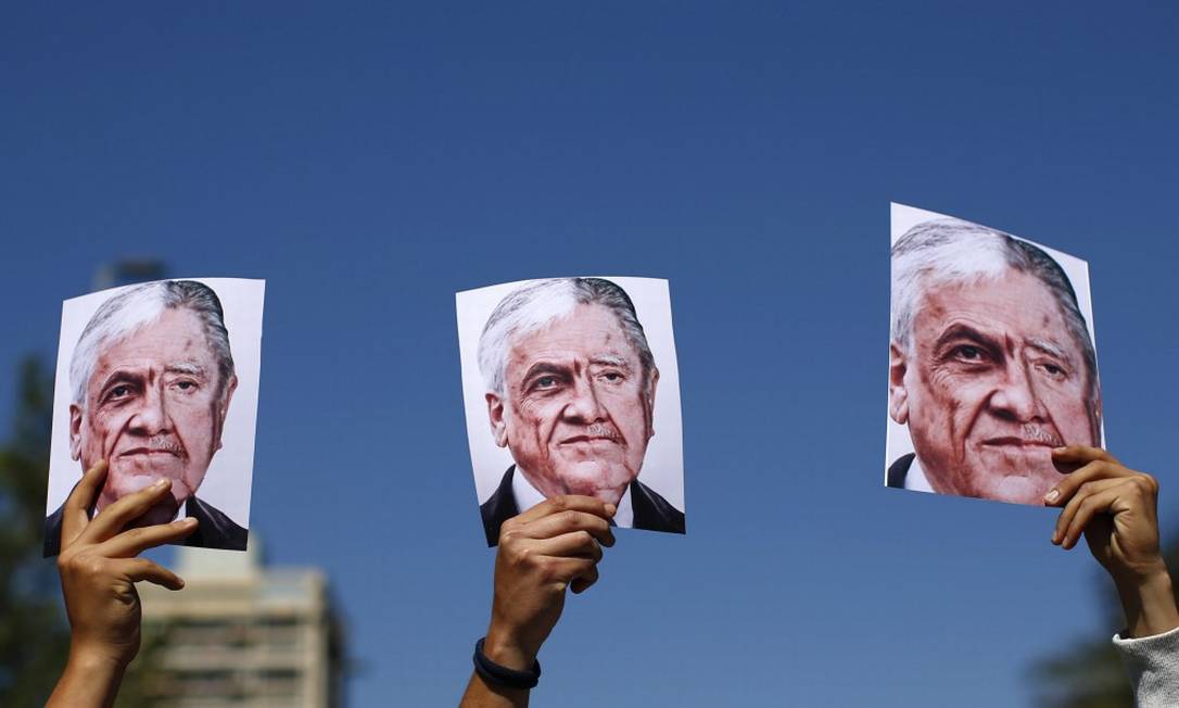Manifestantes carregam cartazes que mostram, lado a lado, os rostos de Sebastián Piñera e Augusto Pinochet Foto: PABLO VERA / AFP