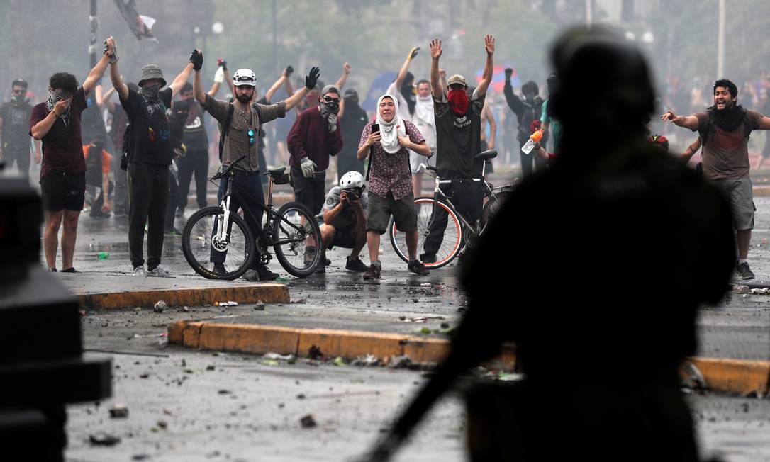 
Manifestantes erguem os braços em frente às forças de segurança em protesto em Santiago: novos confrontos foram registrados nas manifestações, que continuaram nesta quarta apesar do anúncio de um pacote de medidas sociais pelo governo
Foto:
IVAN ALVARADO/REUTERS
