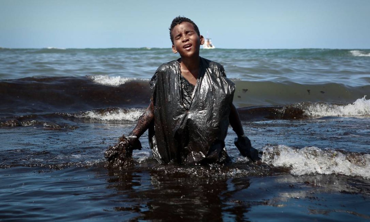 Um menino sai do mar enquanto remove resíduos de óleo derramado na praia de Itapuama, na cidade de Cabo de Santo Agostinho, Pernambuco. Grandes gotas de óleo que mancham mais de 130 praias no nordeste do Brasil começaram a aparecer no início de setembro e, agora, em um trecho de 2.000 km da costa atlântica Foto: Leo Malafaia / AFP - 21/10/2019