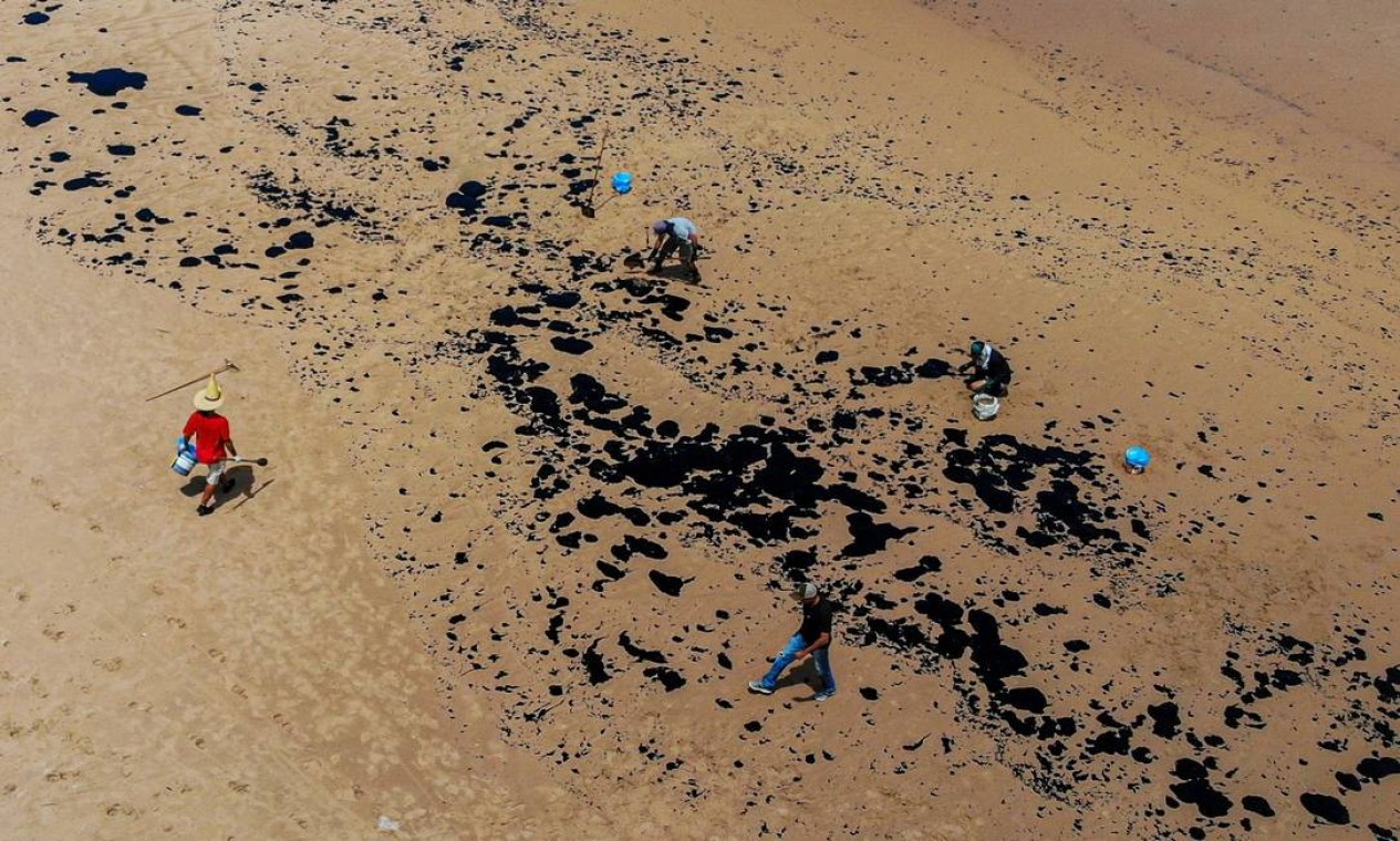 Voluntários removem resíduos de óleo na praia de Jauá, na cidade de Camaçari, Bahia. Origem do material permanece um mistério para pesquisadores e autoridades Foto: Mateus Morbeck / AFP - 17/10/2019
