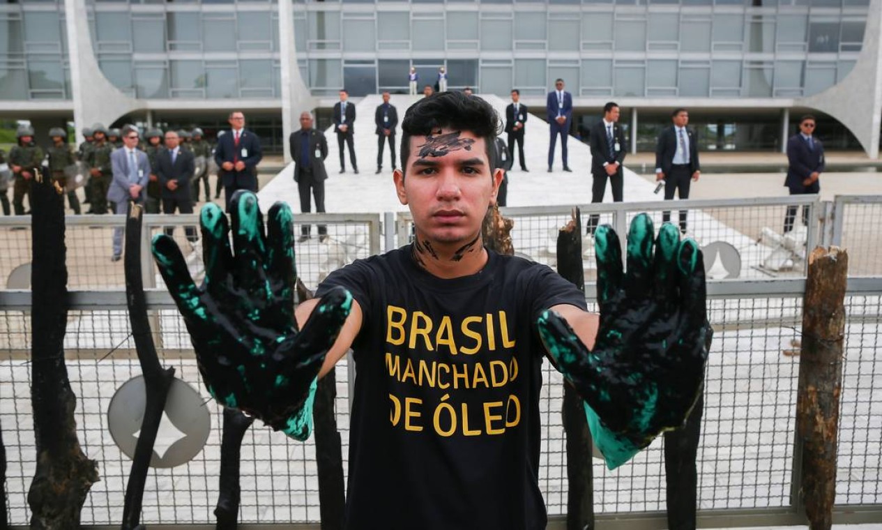 Ativista do Greenpeace protesta com óleo cru falso nas mãos, em frente ao Palácio do Planalto em Brasília, contra o desastre de óleo que manchou centenas de praias no nordeste em 2019 Foto: SERGIO LIMA / AFP - 23/10/2019