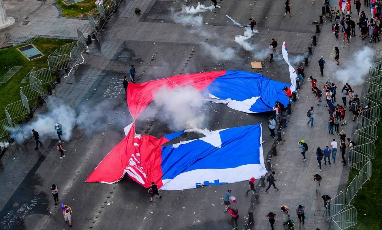 Manifestantes carregam uma bandeira do Chile rasgada. No fim da semana passada, o governo decretou estado de emergência e toque de recolher em várias cidades Foto: MARTIN BERNETTI / AFP