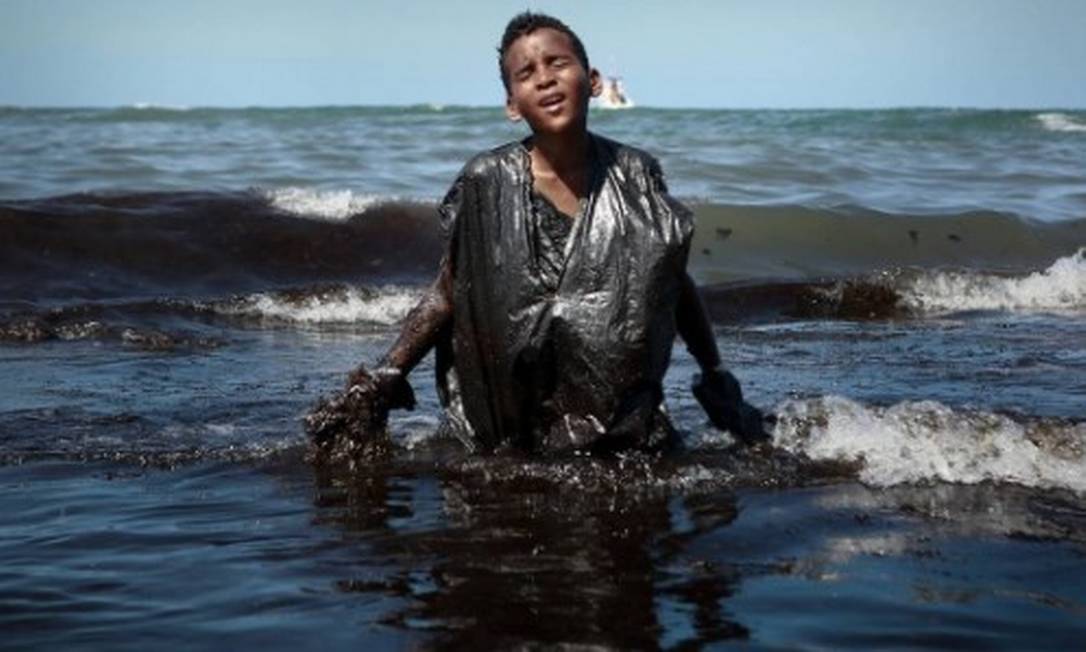 Menino sai do mar repleto de óleo no Cabo de Santo Agostinho, em Pernambuco Foto: Leo Malafaia / AFP