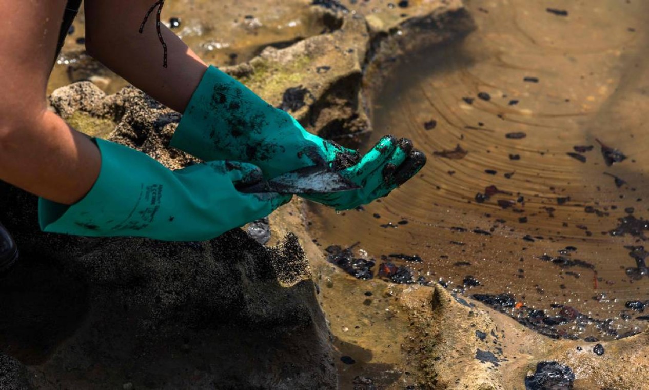 Voluntarios se protegem com luvas de uso doméstico para retirar óleo derramado na praia de Pocas, na cidade de Conde, Bahia Foto: Mateus Morbeck / AFP