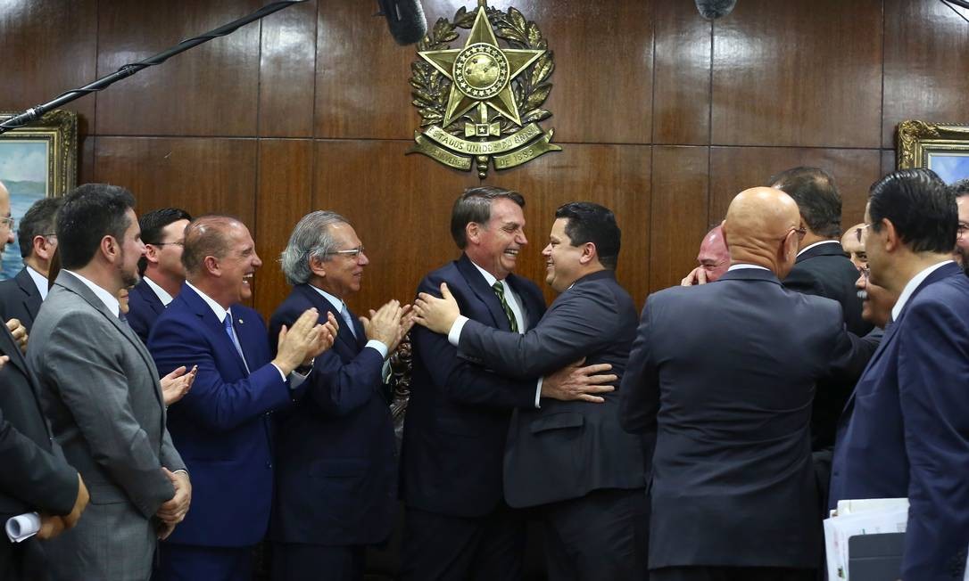 O presidente Jair Bolsonaro abraça o presidente do Senado, Davi Alcolumbre, aplaudido pelos ministro Paulo Guedes e Onyx Lorenzoni, na entrega de propostas econômicas ao Congresso Foto: SERGIO LIMA / AFP