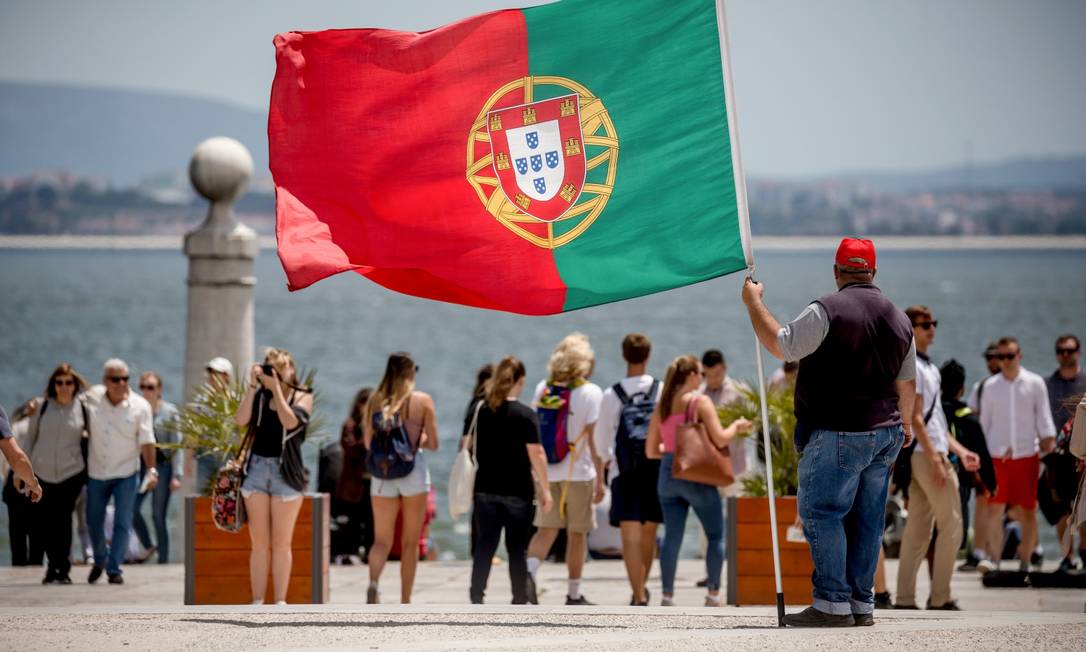 Homem segura bandeira portuguesa enquanto turistas passeiam por Lisboa Foto: MICHAEL KAPPELER / Agência O Globo/31-11-2019