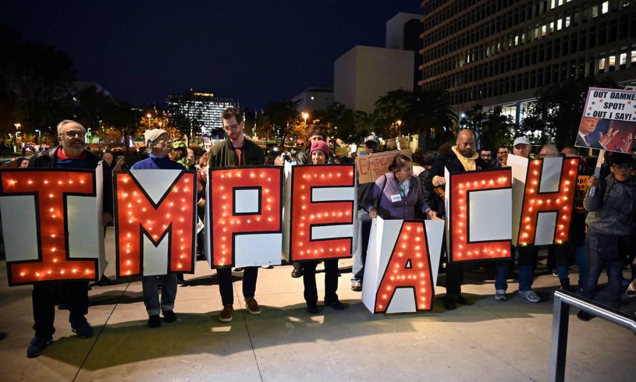 Manifestantes seguram cartazes luminosos pedindo o impeachment de Trump, no prédio da prefeitura de Los Angeles Foto: Robyn Beck / AFP