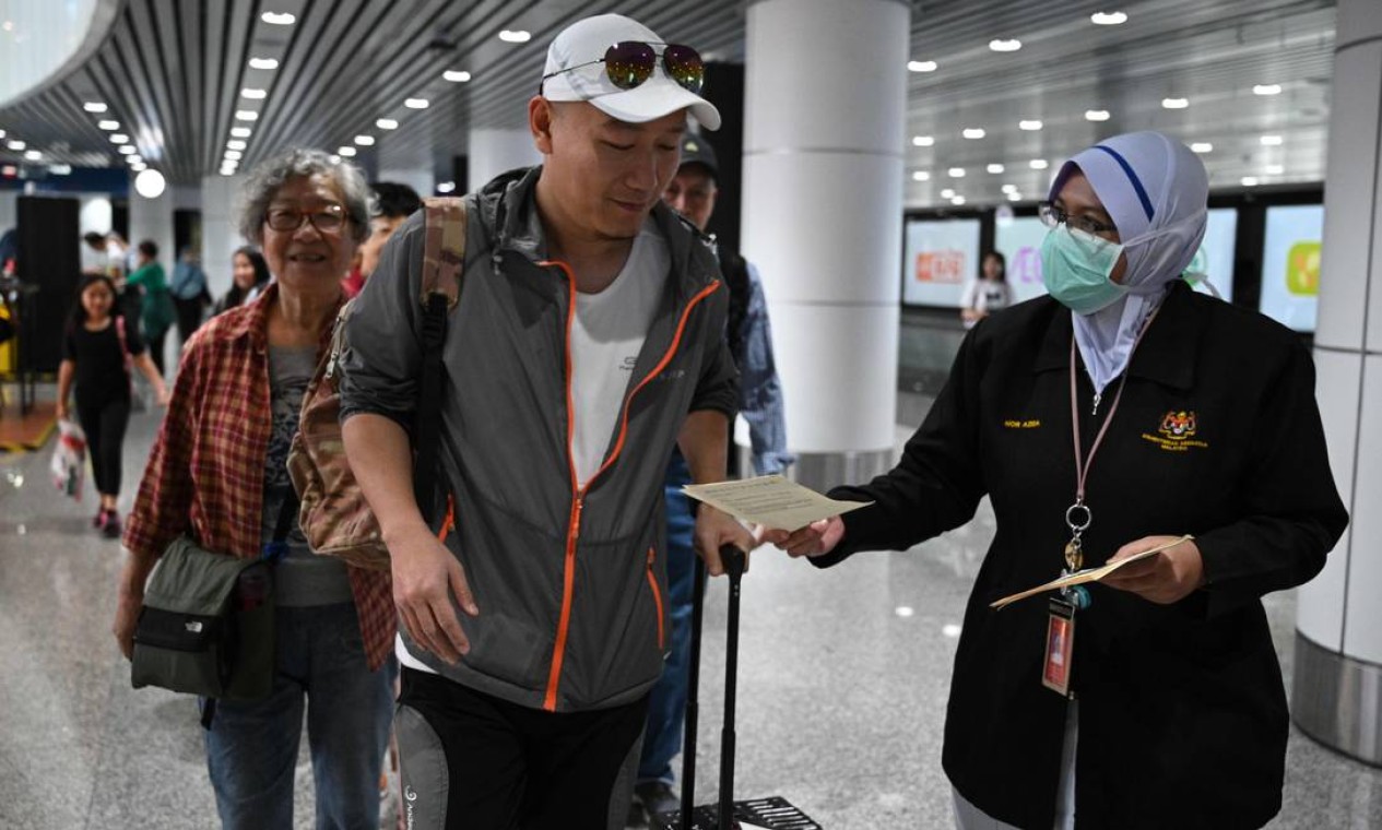 Oficial de saúde da Malásia entrega folhetos a passageiros que chegam no aeroporto internacional de Kuala Lumpur, em Sepang Foto: MOHD RASFAN / AFP