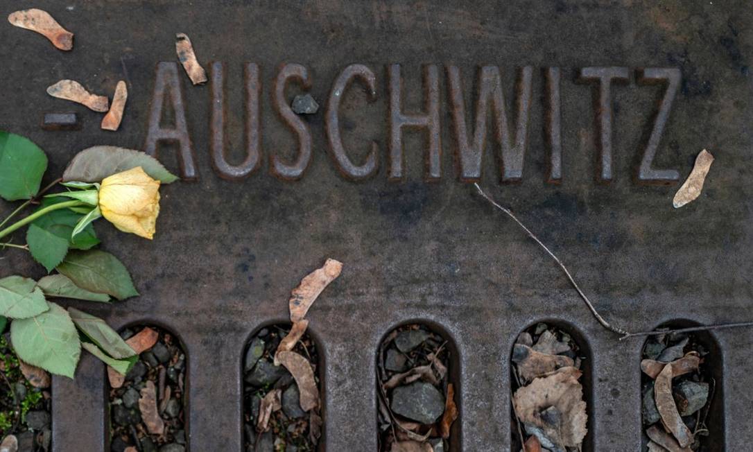 Flor é colocada ao lado de placa que diz "Auschwitz", detalhando os horários de transportes e destinos em um memorial em Berlim Foto: JOHN MACDOUGALL / AFP