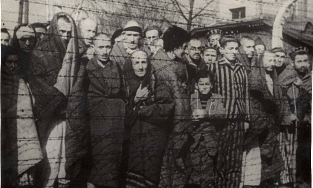 Sobreviventes do Holocausto atrás de cerca de arame farpado no dia da liberação de Auschwitz Foto: Yad Vashen Archives / Via Reuters