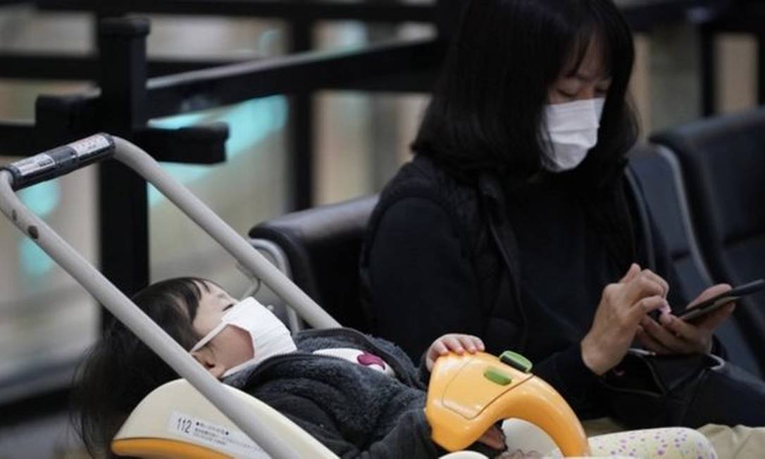 Mulher e criança com máscaras no aeroporto internacional de Tóquio; fábrica de máscaras está trabalhando extra para atender demanda Foto: EPA