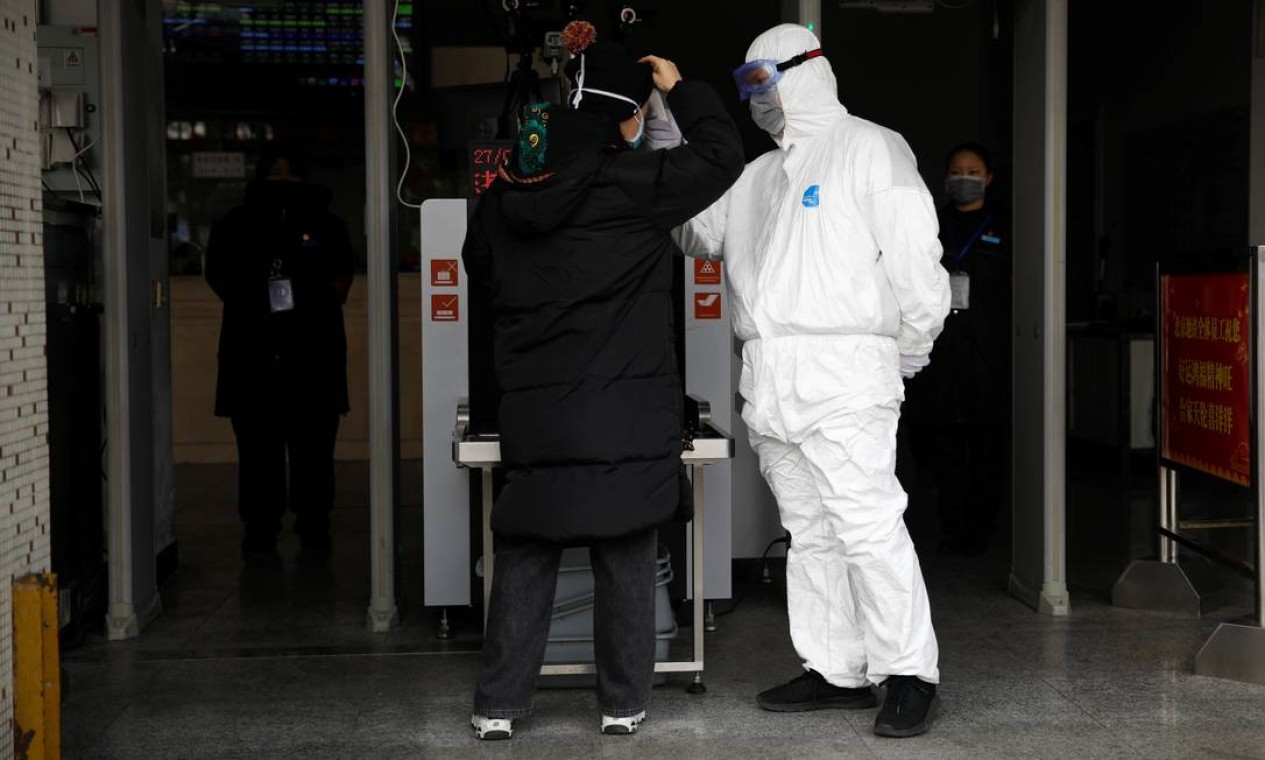 Trabalhador em traje de proteção verifica a temperatura de um homem enquanto entra na estação de metrô de Xizhimen, em Pequim, na China Foto: CARLOS GARCIA RAWLINS / REUTERS