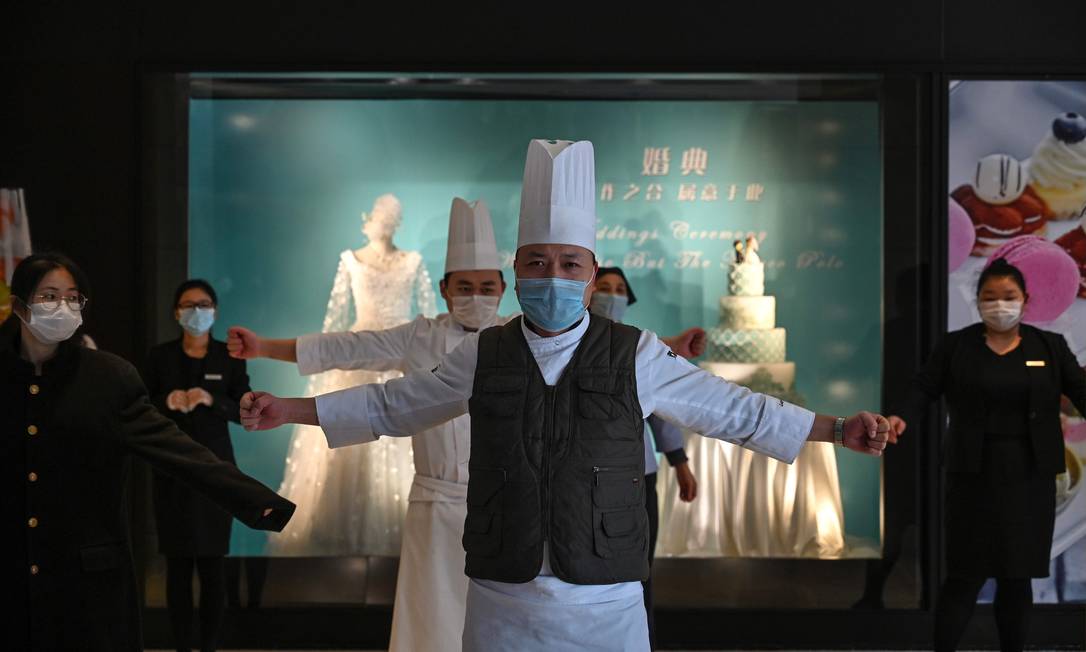 Funcionários usando máscaras protetoras exercitam-se no saguão de um hotel em Wuhan, na província central de Hubei, na China Foto: Hector Retamal / AFP