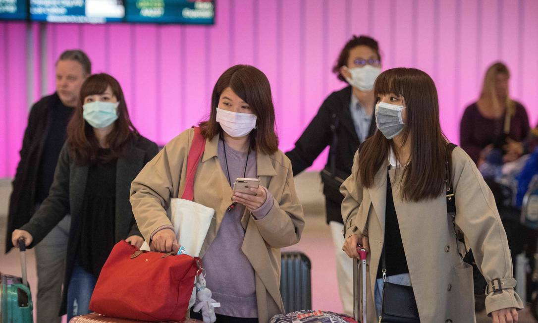 Passageiros chegam ao aeroporto de Los Angeles usando máscaras cirúrgicas para se protegerem do coronavírus Foto: AFP