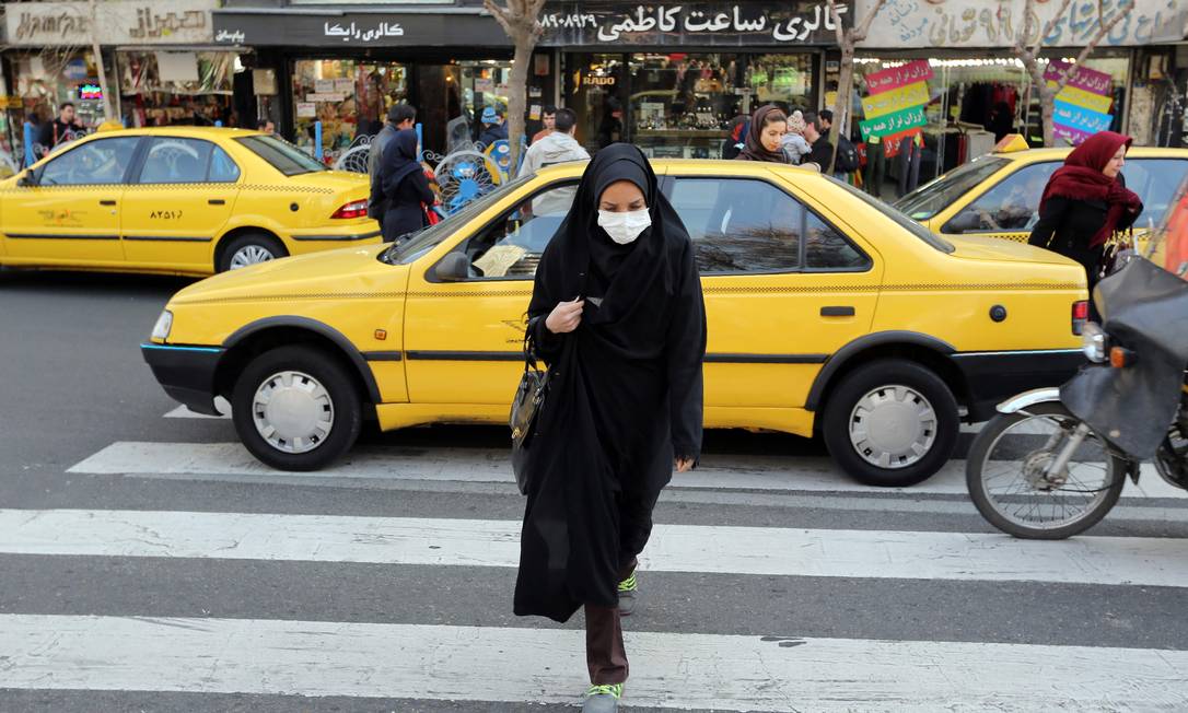 Mulher com máscara no rosto atravessa a rua em Teerã. Novo mecanismo suíço abre caminho para importações de medicamentos, mas compartilhamento de dados com os EUA levanta dúvidas Foto: ATTA KENARE / AFP