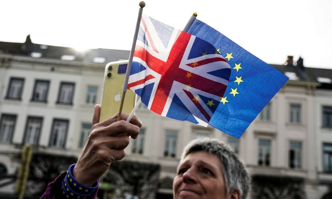 Mulher segura bandeiras do Reino Unido e da União Europeia perto do Parlamento Europeu, em Bruxelas Foto: KENZO TRIBOUILLARD / AFP